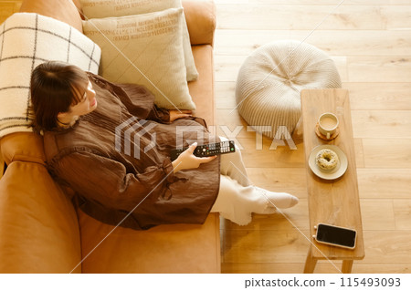 A woman relaxing sitting on a sofa and watching TV A woman relaxing sitting on a sofa and watching TV 115493093