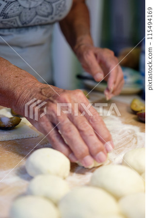 Preparation of homemade fruit dumplings with plums. Czech specialty of sweet good food. Dough on kitchen wooden table with hands. Preparation of homemade fruit dumplings with plums. Czech specialty of sweet good food. Dough on kitchen wooden table with hands. 115494169