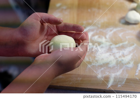 Preparation of homemade fruit dumplings with plums. Czech specialty of sweet good food. Dough on kitchen wooden table with hands. 115494170