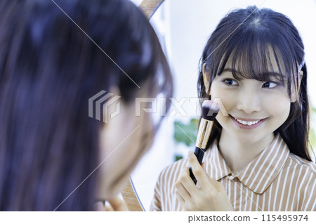 Young woman doing make-up while looking in the mirror Young woman doing make-up while looking in the mirror 115495974