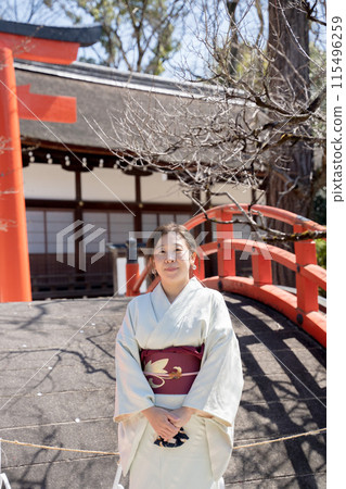 A smiling young woman in a kimono walking through the grounds of a shrine in the spring sunshine 115496259