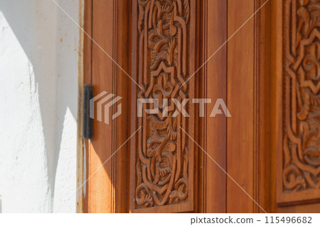 Big old wooden door decorated with various symbolic signs carved directly on the canvas of massif. Example of exterior and interior decoration of entrance lobbies in different cultures around world 115496682