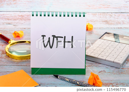 concept image with word WFH. WORK FROM HOME WFH Written on a blank sheet of notepad next to a calculator, stickers, a magnifying glass on old boards concept image with word WFH. WORK FROM HOME WFH Written on a blank sheet of notepad next to a calculator, stickers, a magnifying glass on old boards 115496770
