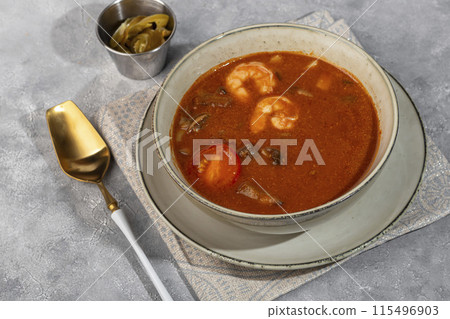Tom yum soup with seafood, capers added nearby. 115496903