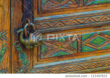 An antique padlock in the shape of a one-humped dromedary camel guards the tranquility on a beautifully decorated door with carved designs and ornaments 115497632