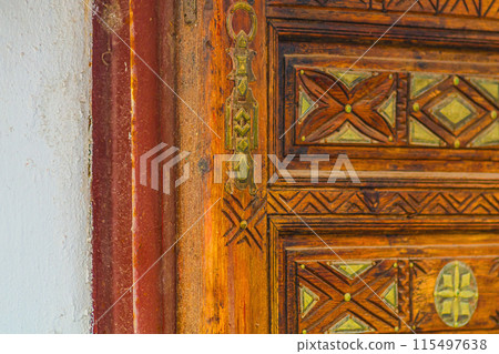Big old wooden door decorated with various symbolic signs carved directly on the canvas of massif. Example of exterior and interior decoration of entrance lobbies in different cultures around world 115497638