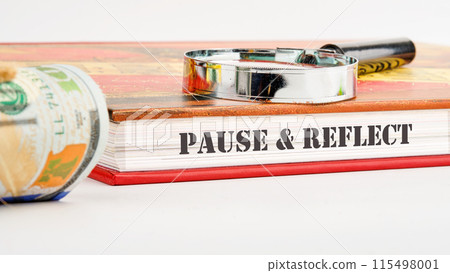 Pause and reflect word on the end of the book on a white background and compositions with a magnifying glass and money 115498001