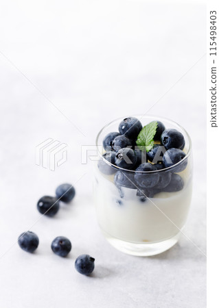 Ripe organic blueberries with yogurt in a glass on white stone table background. Selective focus. Ripe organic blueberries with yogurt in a glass on white stone table background. Selective focus. 115498403