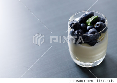 Ripe organic blueberries with yogurt in a glass on black stone table background. Selective focus. 115498410