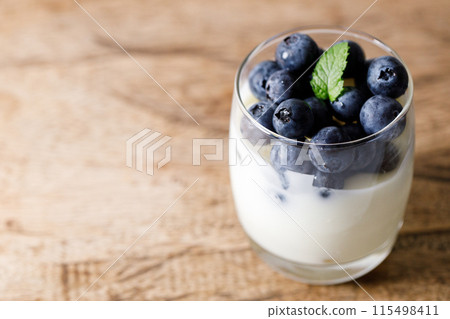 Ripe organic blueberries with yogurt in a glass on rustic wooden table background. Selective focus. Ripe organic blueberries with yogurt in a glass on rustic wooden table background. Selective focus. 115498411
