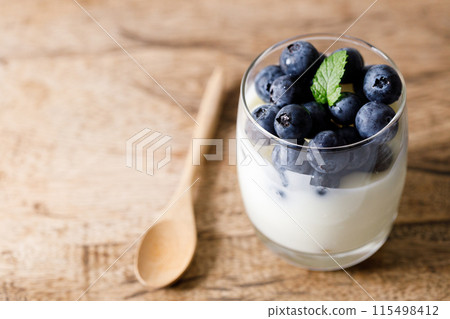 Ripe organic blueberries with yogurt in a glass on rustic wooden table background. Selective focus. 115498412