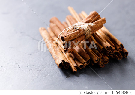 Cinnamon sticks dried tree bark spice on black stone table background. Selective focus. Cinnamon sticks dried tree bark spice on black stone table background. Selective focus. 115498462