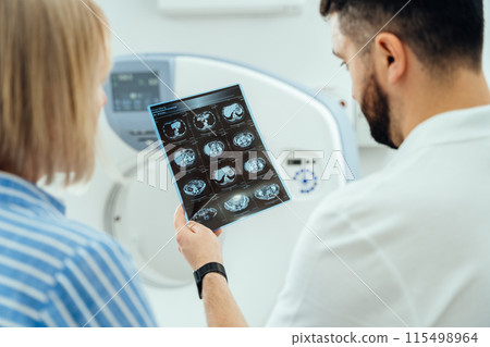 A man and a woman are looking at a medical image of a brain. The man is holding the image up to the woman's face 115498964