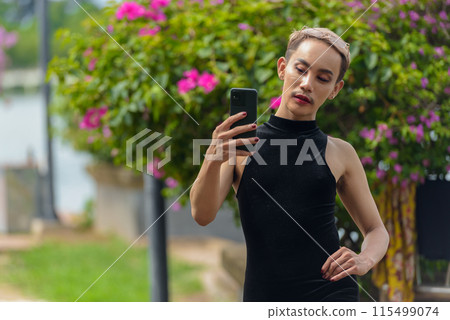 Queer LGBT community supporter man with mustache wearing jumpsuit using phone outdoors in park Queer LGBT community supporter man with mustache wearing jumpsuit using phone outdoors in park 115499074