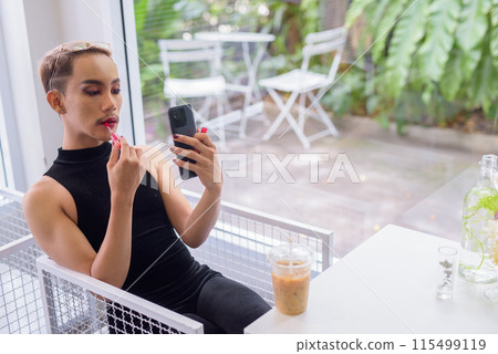 Beautiful Asian queer LGBT community supporter man sitting in coffee shop applying lipstick 115499119
