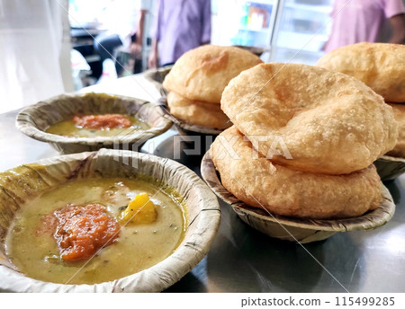 Bedmi puri and potato curry kept in a leaf container (Dona) on the table 115499285