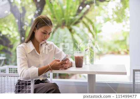 Asian student takes a break at a modern cafe and checking her smartphone Asian student takes a break at a modern cafe and checking her smartphone 115499477