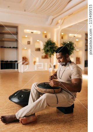Vertical portrait of meditate African man in trance enjoying playing ethnic music on glucophone using sticks sitting on floor in lotus pose. Concept of mindfulness, tranquility, harmony, sound therapy 115499555