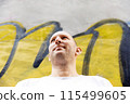 Bald man in white t-shirt looking sideways, colorful graffiti background, urban setting 115499605