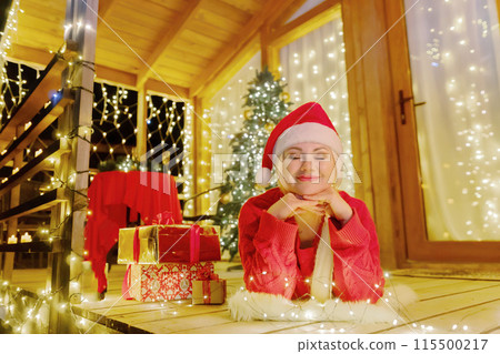 Woman in Santa hat by Christmas tree. Festive setting. Illustrating holiday cheer and celebration. She is posing for a picture, and there are presents nearby, adding to the festive atmosphere. Woman in Santa hat by Christmas tree. Festive setting. Illustrating holiday cheer and celebration. She is posing for a picture, and there are presents nearby, adding to the festive atmosphere. 115500217
