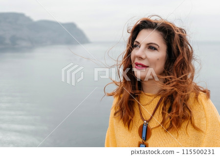 Portrait windswept hair happy woman against a backdrop of mountains and sea. Daylight illuminates the tranquil outdoor setting 115500231
