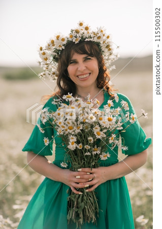 Happy woman in a field of daisies with a wreath of wildflowers on her head. woman in a green dress in a field of white flowers. Charming woman with a bouquet of daisies, tender summer photo Happy woman in a field of daisies with a wreath of wildflowers on her head. woman in a green dress in a field of white flowers. Charming woman with a bouquet of daisies, tender summer photo 115500302