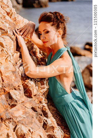 Woman green dress sea. Woman in a long mint dress posing on a beach with rocks on sunny day. Girl on the nature on blue sky background. Woman green dress sea. Woman in a long mint dress posing on a beach with rocks on sunny day. Girl on the nature on blue sky background. 115500305