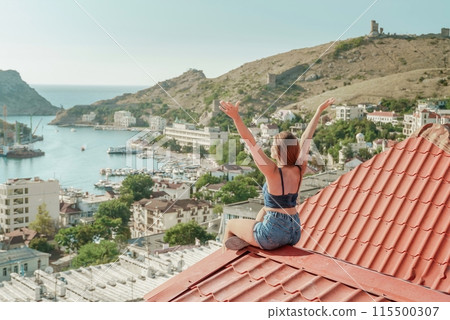 Woman sits on rooftop with outstretched arms, enjoys town view and sea mountains. Peaceful rooftop relaxation. Below her, there is a town with several boats visible in the water Woman sits on rooftop with outstretched arms, enjoys town view and sea mountains. Peaceful rooftop relaxation. Below her, there is a town with several boats visible in the water 115500307