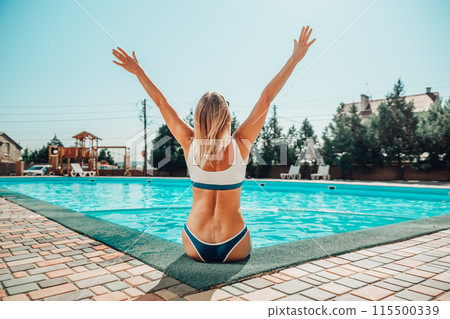 A woman is sitting in a pool with her arms raised in the air. Scene is joyful and carefree. A woman is sitting in a pool with her arms raised in the air. Scene is joyful and carefree. 115500339