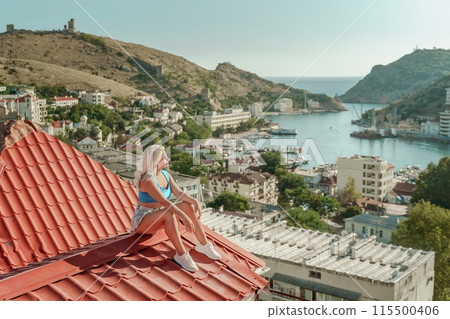 Woman sits on rooftop, enjoys town view and sea mountains. Peaceful rooftop relaxation. Below her, there is a town with several boats visible in the water. Rooftop vantage point. Woman sits on rooftop, enjoys town view and sea mountains. Peaceful rooftop relaxation. Below her, there is a town with several boats visible in the water. Rooftop vantage point. 115500406