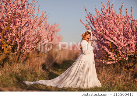 Woman blooming peach orchard. Against the backdrop of a picturesque peach orchard, a woman in a long white dress enjoys a peaceful walk in the park, surrounded by the beauty of nature. Woman blooming peach orchard. Against the backdrop of a picturesque peach orchard, a woman in a long white dress enjoys a peaceful walk in the park, surrounded by the beauty of nature. 115500415