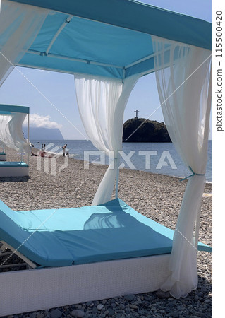 A blue and white beach umbrella with white curtains is set up on a beach 115500420
