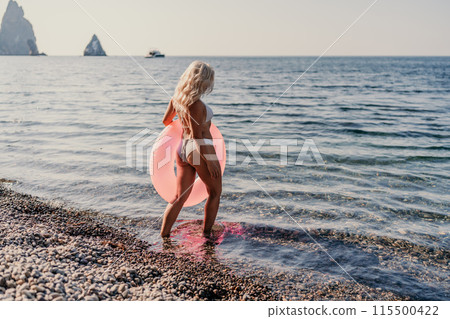 A woman in a bikini is standing in the ocean with a pink inflatable tube 115500422