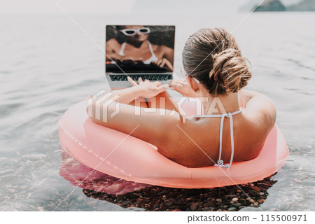 A woman is sitting on a pink inflatable raft in the ocean, reading a laptop. Concept of relaxation and leisure, as the woman enjoys her time by the water while working or browsing the internet. A woman is sitting on a pink inflatable raft in the ocean, reading a laptop. Concept of relaxation and leisure, as the woman enjoys her time by the water while working or browsing the internet. 115500971