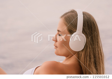 A woman wearing headphones is laying on a beach 115501012