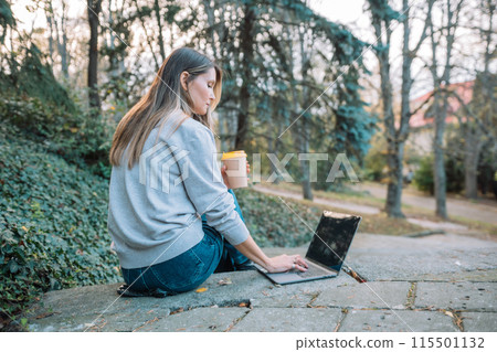 A woman is sitting on a stone ledge with a laptop and a cup of coffee. She is working or studying, as she is focused on her laptop. Concept of productivity and concentration. A woman is sitting on a stone ledge with a laptop and a cup of coffee. She is working or studying, as she is focused on her laptop. Concept of productivity and concentration. 115501132