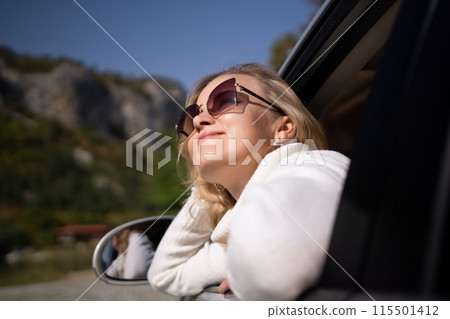 A blonde woman in a white sweater and jeans is driving. Happy woman sitting in the car. 115501412