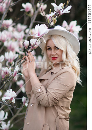 Magnolia flowers woman. A blonde woman wearing a white hat stands in front of a tree with pink flowers. She has a smile on her face and she is enjoying the beautiful scenery. 115501465