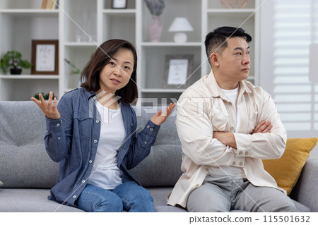Asian couple sitting on a couch during a disagreement, showcasing relationship conflict and communication issues. 115501632