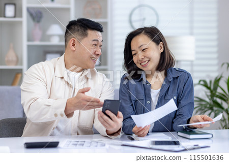 Smiling couple managing their finances at home, discussing budget plans with a smartphone and paperwork. Concept of teamwork, financial planning, and domestic lifestyle. Smiling couple managing their finances at home, discussing budget plans with a smartphone and paperwork. Concept of teamwork, financial planning, and domestic lifestyle. 115501636