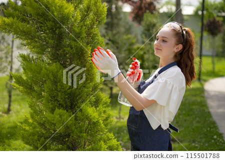 Side view of young girl with red hair spraying trees, looking up. Concept of taking care of plants. 115501788
