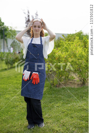 Front view of slim girl standing, wotking in garden, looking at camera. Concept of taking care of nature. Front view of slim girl standing, wotking in garden, looking at camera. Concept of taking care of nature. 115501812