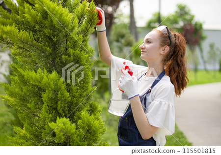 Side view of girl with red hair standing, working in garden, looking forward. Concept of taking care of plants. 115501815