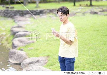 A young man operating a smartphone by the water 115501835