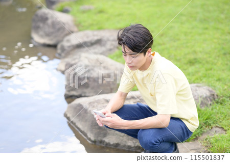 A young man operating a smartphone by the water 115501837
