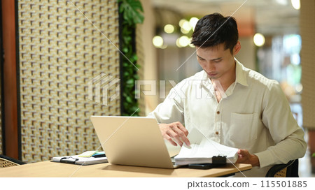 Millennial businessman using laptop and working with financial document in modern office lounge Millennial businessman using laptop and working with financial document in modern office lounge 115501885