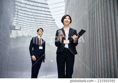 A businesswoman in a suit operating a smartphone while moving around the office A businesswoman in a suit operating a smartphone while moving around the office 115502595