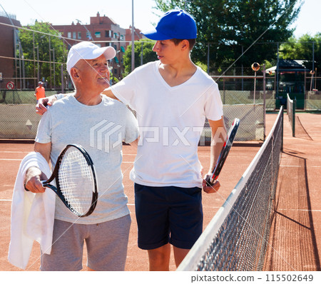 Grandfather and grandson talking on court playing tennis 115502649