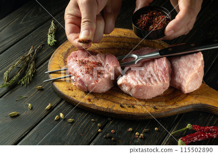 Cooking a juicy beef steak. Chef hands adding dry spices to the meat on the countertop before grilling. Picnic preparation concept Cooking a juicy beef steak. Chef hands adding dry spices to the meat on the countertop before grilling. Picnic preparation concept 115502890