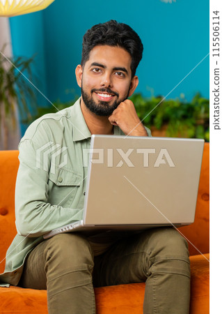 Young man freelancer sitting on couch with laptop pc after finishing work in living room at home 115506114
